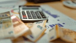 A calculator and several euro banknotes on top of financial charts and documents.