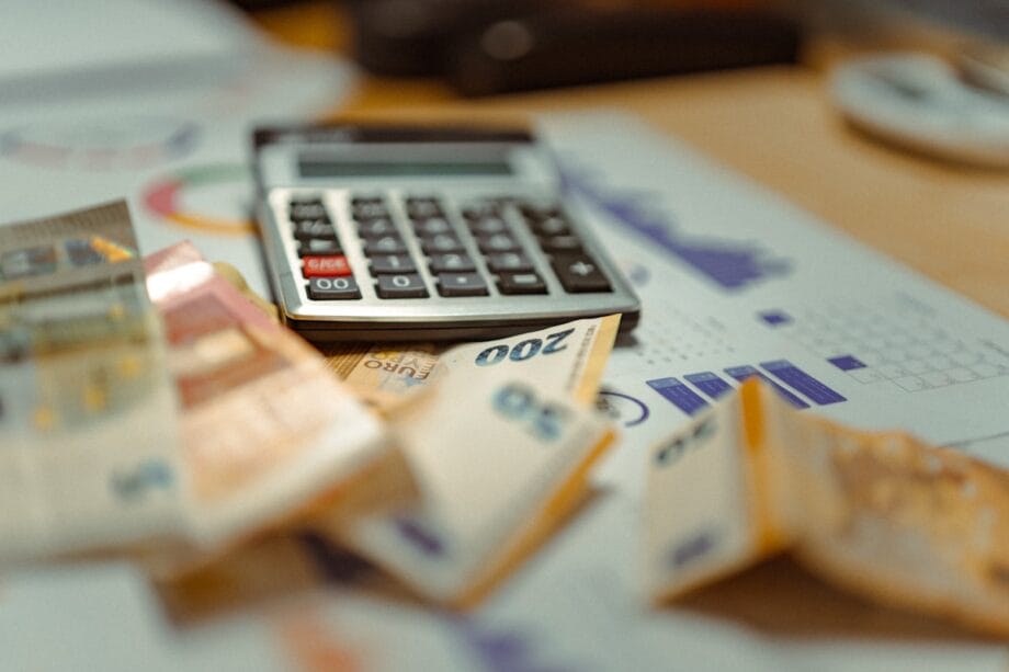 A calculator and several euro banknotes on top of financial charts and documents.