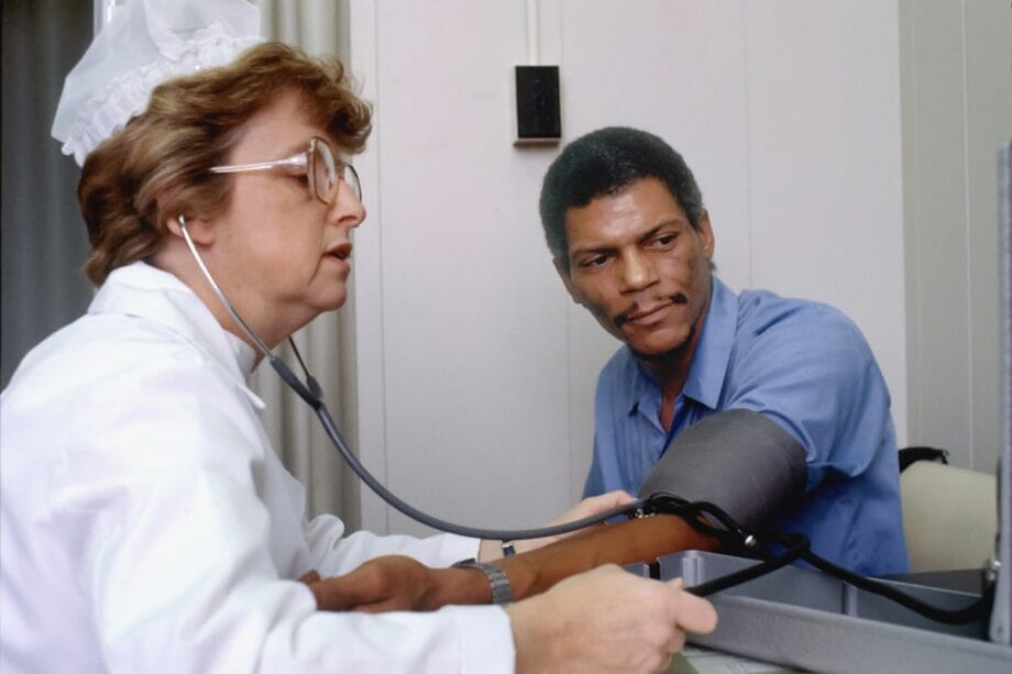 A nurse measures a mans blood pressure with a sphygmomanometer in a clinical setting.