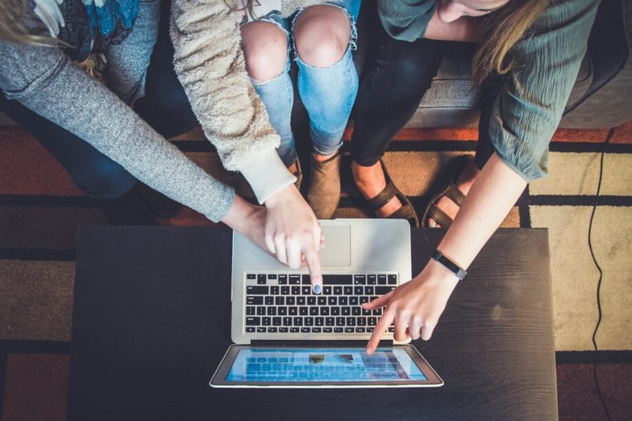 Three people sitting on a couch point at a laptop screen on a table, collaborating on something together.