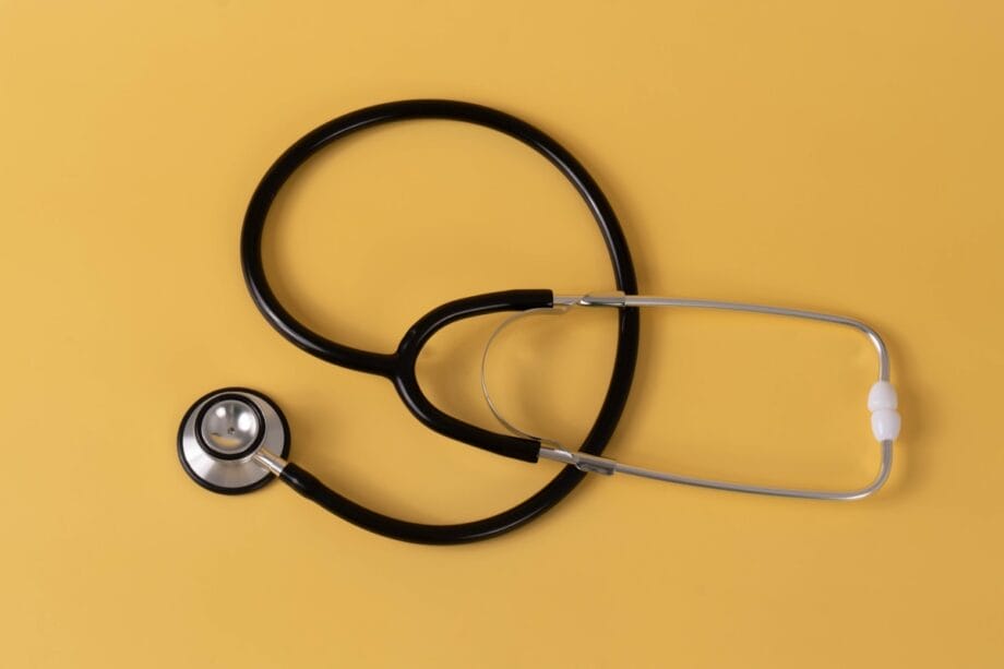 A black and silver stethoscope is arranged on a plain yellow background.