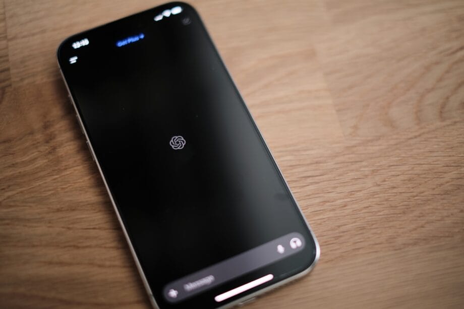 A smartphone displaying the ChatGPT loading screen rests on a wooden surface.