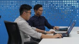 two men sitting at a table with laptops