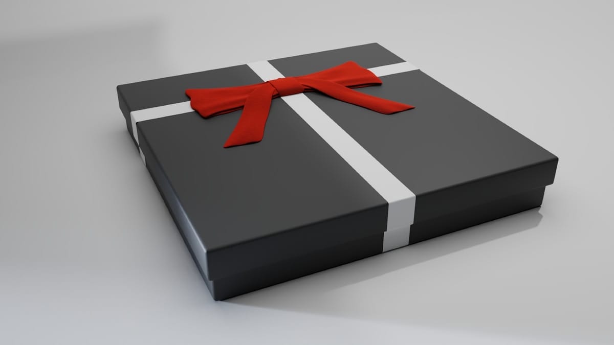 A square black gift box with a white ribbon and a red bow, placed on a plain light-colored surface.