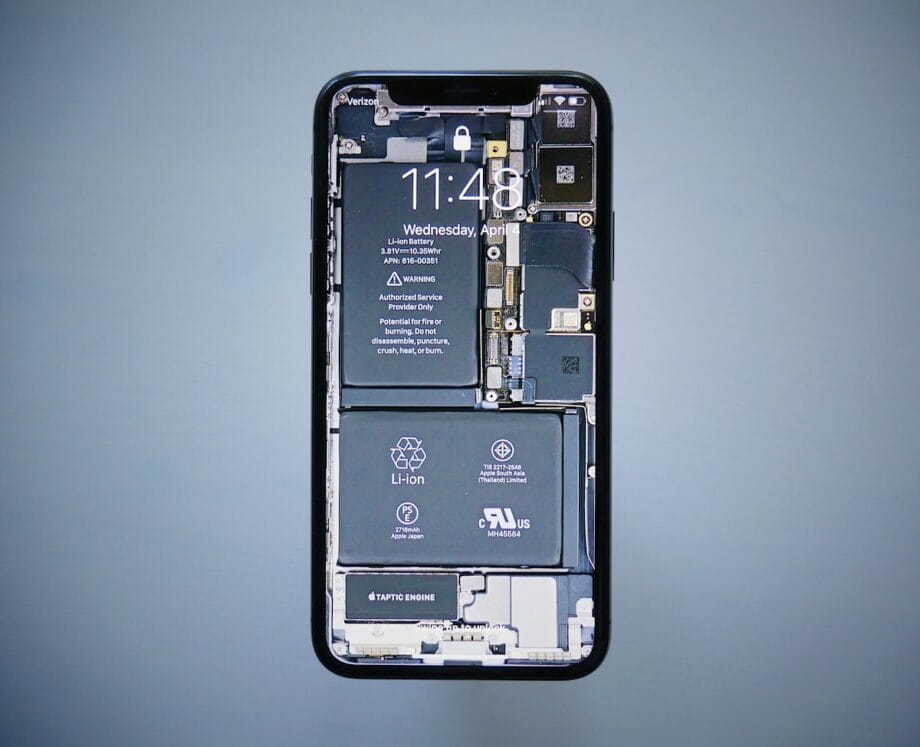 A smartphone with a wallpaper displaying internal components, including the battery and circuitry, against a plain gray background.