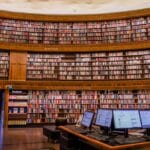 A large, circular library with rows of bookshelves and a desk with computer monitors in the foreground.