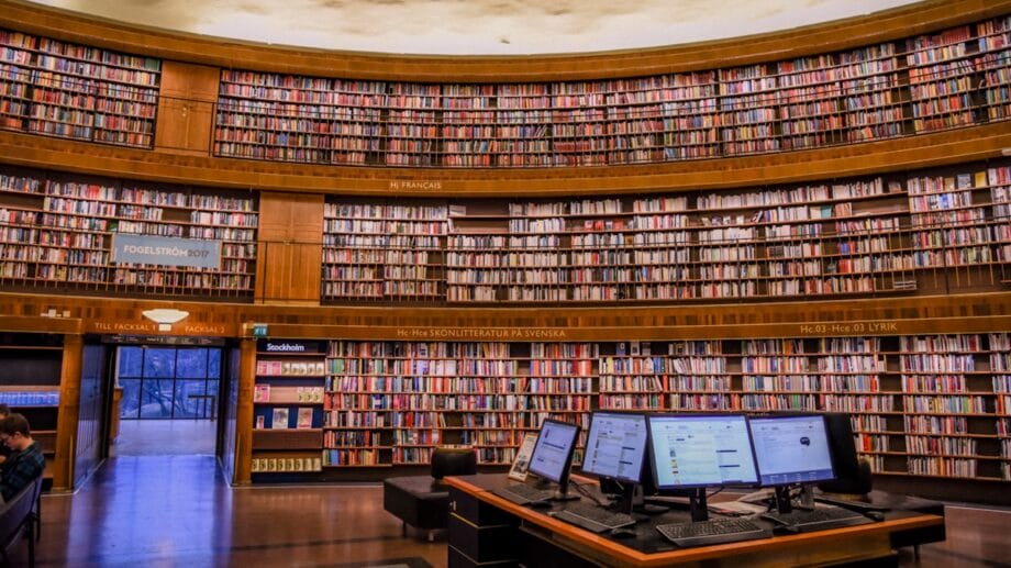 A large, circular library with rows of bookshelves and a desk with computer monitors in the foreground.