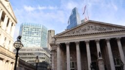 A neoclassical building with columns in front of modern glass skyscrapers under a blue sky with some clouds.
