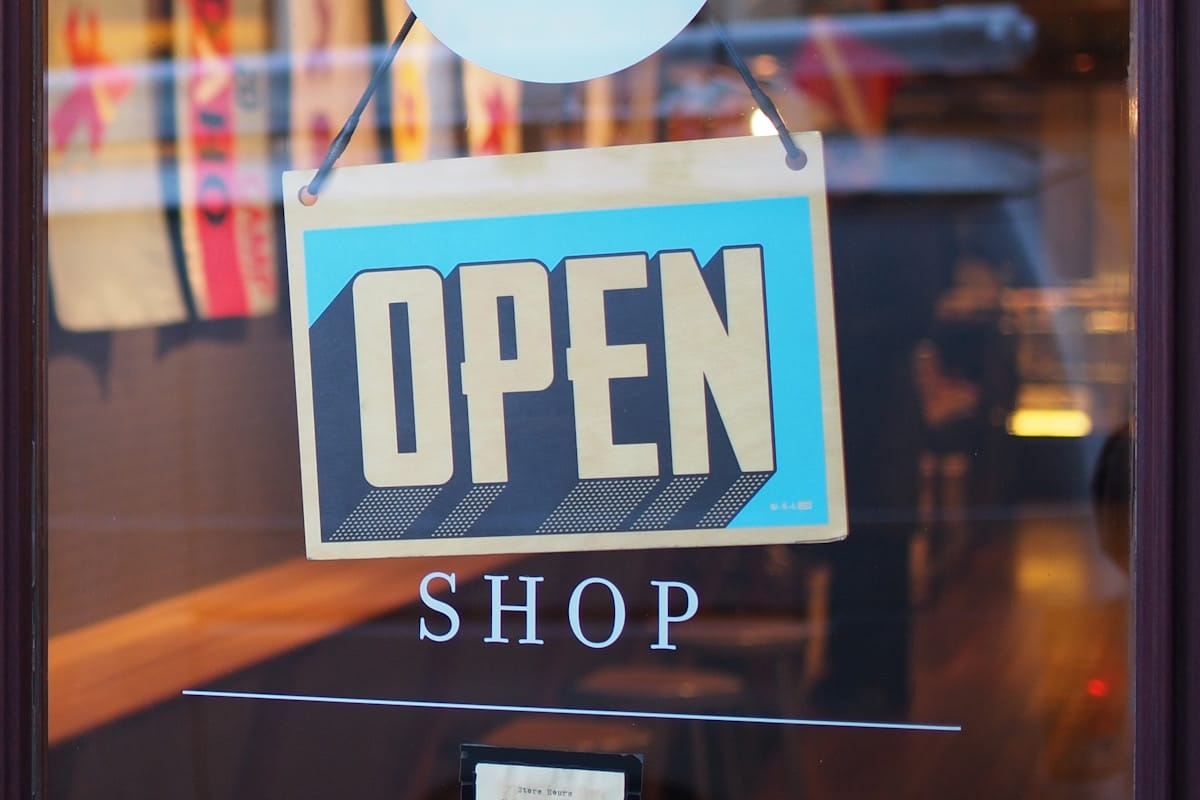 A sign with the word OPEN hangs on a glass door above the word SHOP, indicating the store is open for business.