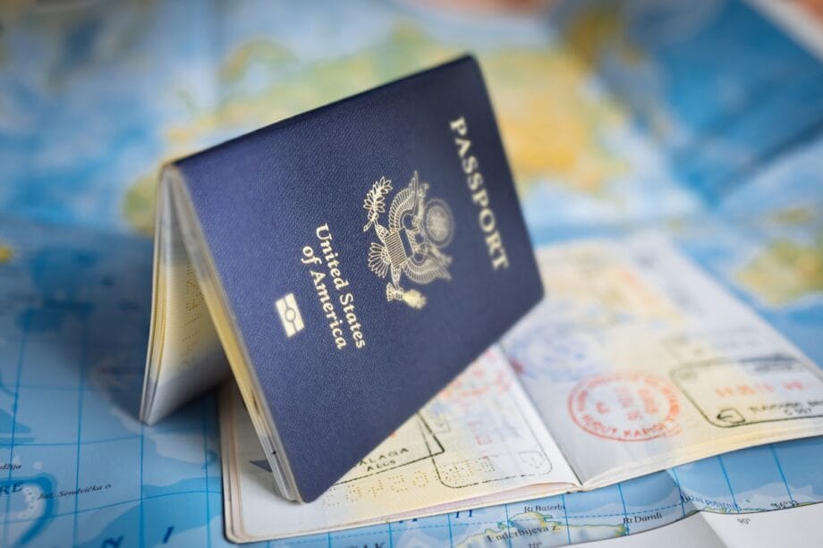 A United States passport standing open on top of a map, with visible passport stamps and travel visas.