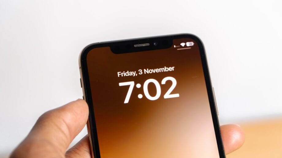 A hand holding a smartphone displaying the time 7:02 and the date Friday, 3 November on the lock screen.