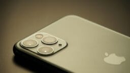 Close-up of the back of a silver iPhone showing three camera lenses and the Apple logo on a neutral background.