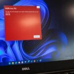 A laptop screen displays a red warning popup about a malicious file over a Windows 11 desktop background.