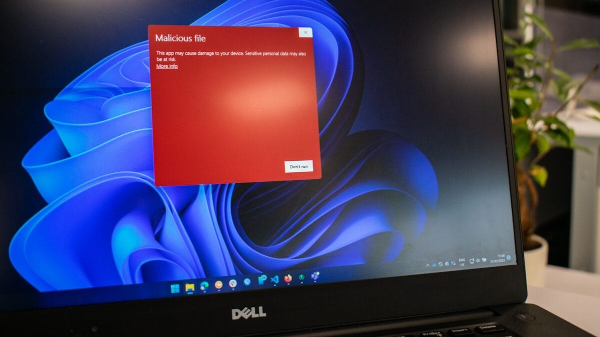 A laptop screen displays a red warning popup about a malicious file over a Windows 11 desktop background.