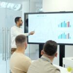Man presenting charts on a large screen to audience.