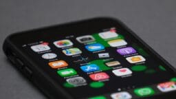 A close-up of a smartphone displaying various app icons on its home screen, including Maps, Photos, and Weather.