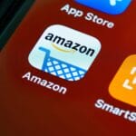 Close-up of a smartphone screen showing the Amazon app icon, featuring a shopping cart and the Amazon logo.