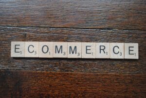 The word ECOMMERCE spelled out with Scrabble letter tiles on a dark wooden surface.