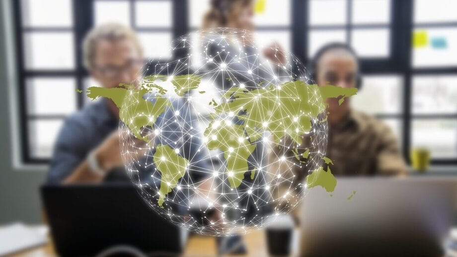 Three people work at laptops with a digital globe and network connections overlayed in the foreground.