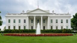 The White House with a central fountain and red flowers on a cloudy day.