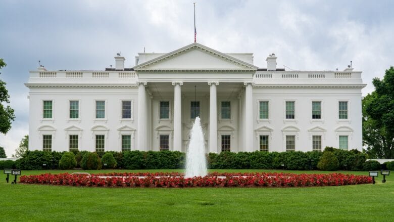 The White House with a central fountain and red flowers on a cloudy day.