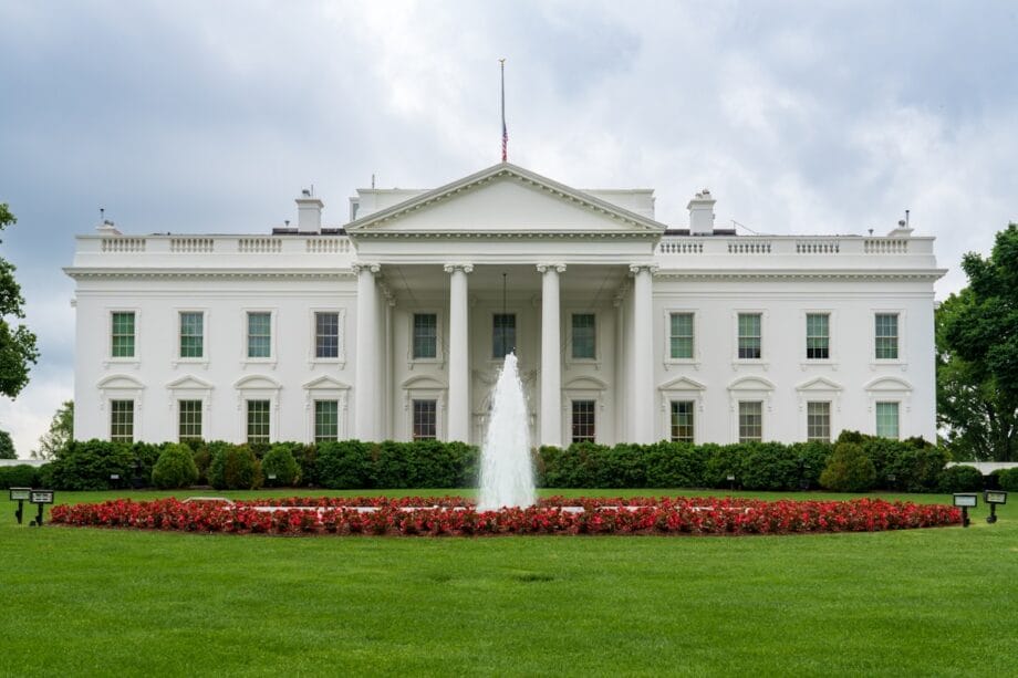 The White House with a central fountain and red flowers on a cloudy day.