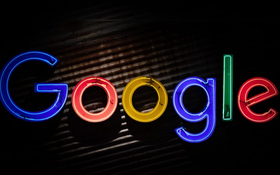 A neon sign displays the word Google in colorful, illuminated letters against a dark background.
