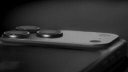 Close-up of a smartphone’s rear camera module with three lenses and a flash, set against a dark, blurred background.