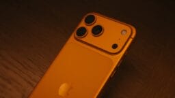 Back of an orange smartphone with three cameras.