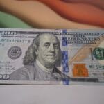 A close-up of a U.S. one hundred dollar bill featuring Benjamin Franklin and security features, lying on a flat surface.