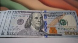 A close-up of a U.S. one hundred dollar bill featuring Benjamin Franklin and security features, lying on a flat surface.