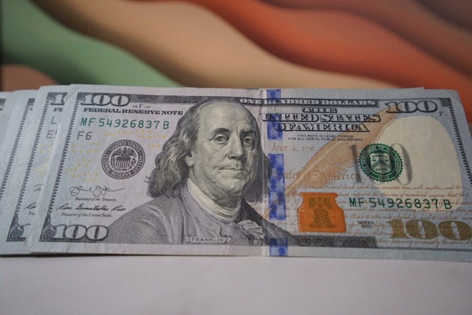 A close-up of a U.S. one hundred dollar bill featuring Benjamin Franklin and security features, lying on a flat surface.