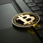 A gold Bitcoin token placed on a laptop keyboard, symbolizing cryptocurrency and digital transactions.