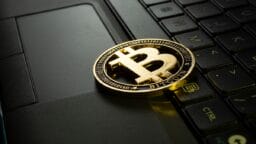 A gold Bitcoin token placed on a laptop keyboard, symbolizing cryptocurrency and digital transactions.