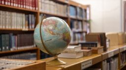 A globe sitting on top of a book shelf in a library
