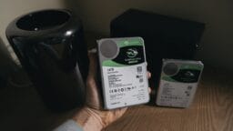 A person holds a 14TB Seagate Barracuda hard drive; another similar hard drive rests on a wooden surface nearby.