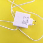 A white USB wall charger with a European plug and cable is placed on a yellow background.