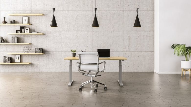 Minimalist office with a desk, white chair, laptop, three black pendant lights, wall shelves, and a potted plant on a concrete floor.