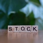 Scrabble tiles on a wooden surface spell the word STOCK with a blurred green background.