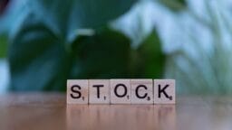Scrabble tiles on a wooden surface spell the word STOCK with a blurred green background.