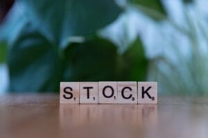 Scrabble tiles on a wooden surface spell the word STOCK with a blurred green background.