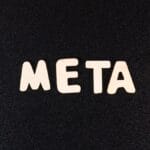 The word META spelled out in white wooden letters on a textured black background.