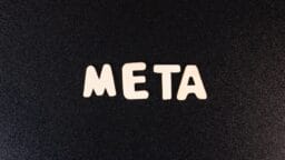 The word META spelled out in white wooden letters on a textured black background.