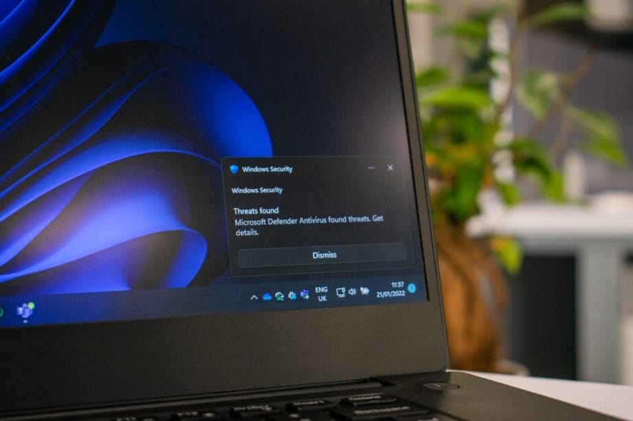 A laptop screen displays a Windows Security notification about detected threats on the system, with an option to dismiss the alert.
