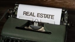 A sheet of paper in a vintage typewriter displays the words REAL ESTATE in bold, uppercase letters.