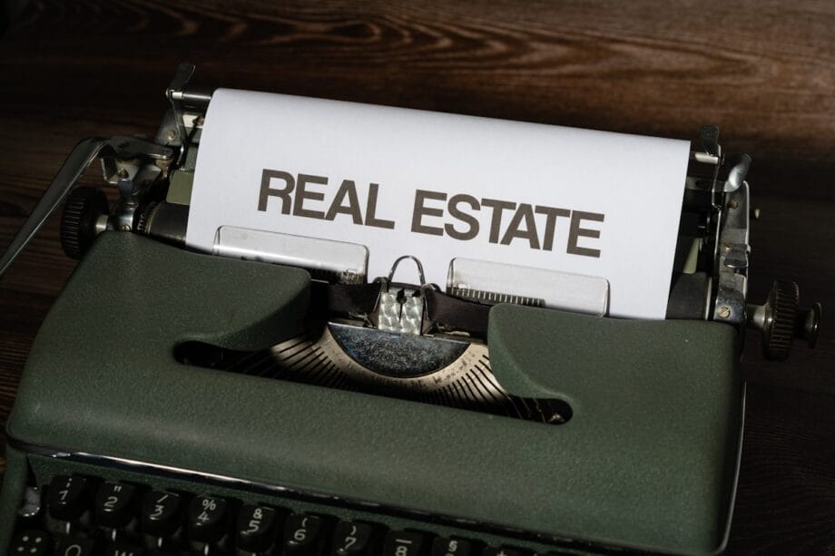 A sheet of paper in a vintage typewriter displays the words REAL ESTATE in bold, uppercase letters.