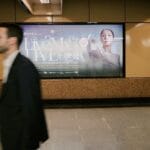 People walk past illuminated advertisements in a subway station.