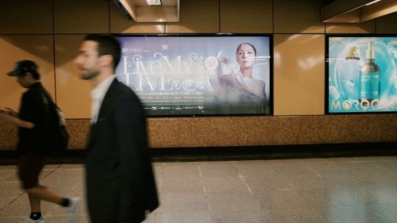 People walk past illuminated advertisements in a subway station.