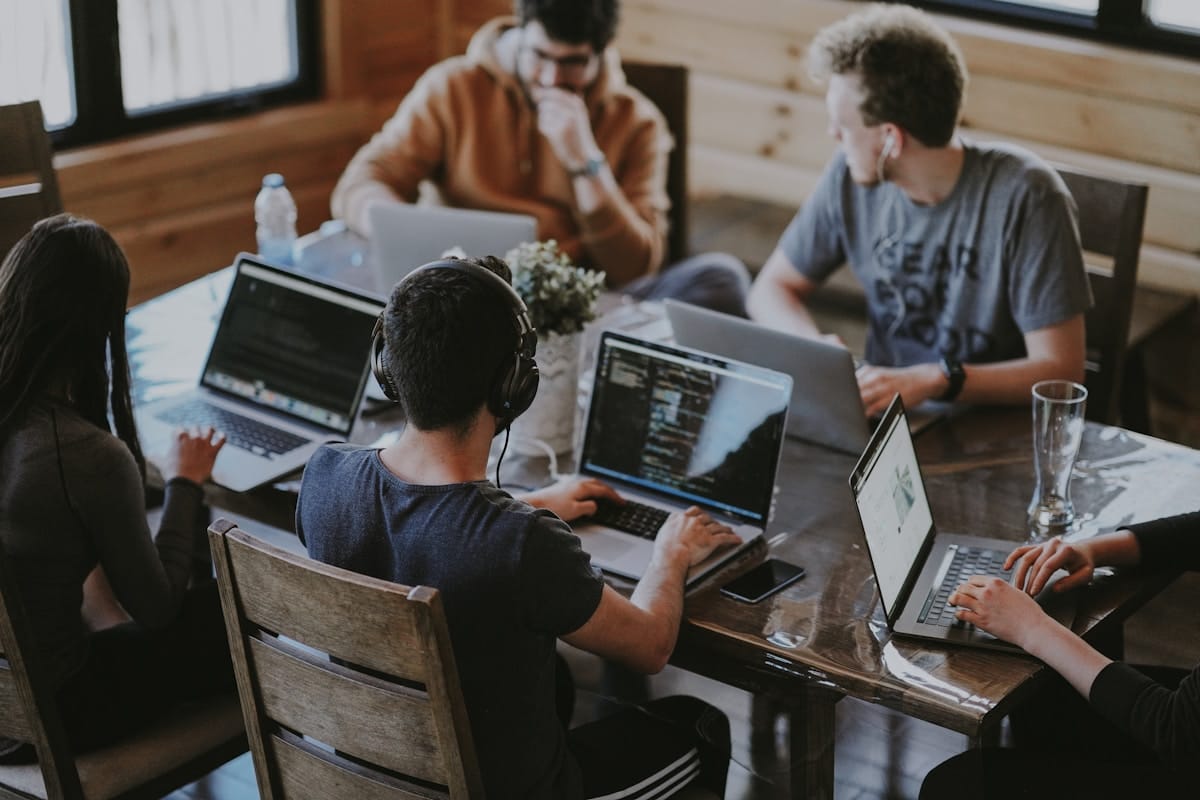 Five people working on laptops around a table in a casual, collaborative office setting with natural light.