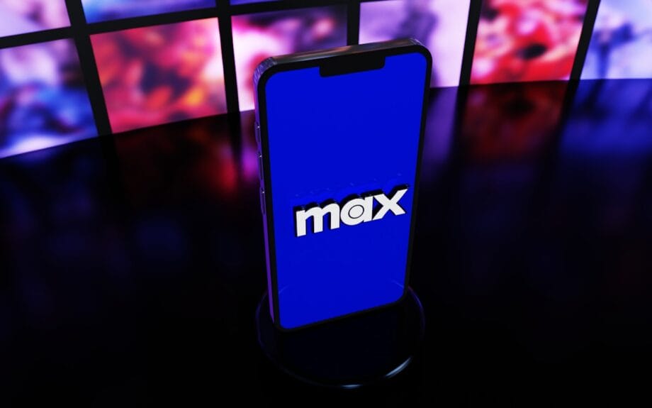 A smartphone displays the Max streaming service logo on its screen, with blurred screens in the background.